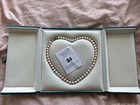 Pearl necklace arranged in a heart shape inside an open blue jewelry box, with an auction card placed in the center.