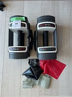 Two PowerBlock Sport 24 adjustable dumbbells with four resistance bands arranged on a light wood floor