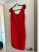 Front view of the red cocktail dress hanging on door, showing V neckline and sleeveless design.