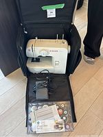 Singer machine installed in black rolling carry case with foot pedal and clear organizer visible