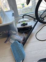 Steam mop with hose, blue cleaning pad attached, and plastic container visible in background