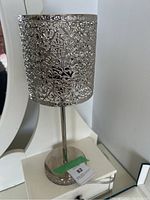 Full view of the silver filigree table lamp showing the detailed metal patterned shade and metal base with stem.