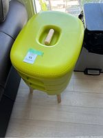 Full front and top view of bright green Urbalive vermi-composter with wooden legs and handle on top in natural light on floor.