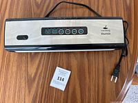 Front view of Maidong Etunsia vacuum sealer with control buttons, power cord and wood floor background.