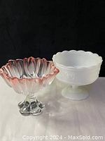 Image showing both candy dishes side by side on a reflective surface against black background. Pink tulip glass dish on the left, white milk glass on the right.