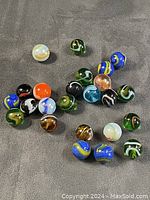 Photo showing 22 assorted glass marbles of various colors and swirl patterns spread out on cloth surface.