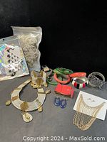 Photo shows various bracelets (resin bangles, metal bracelets), a gold-tone necklace with hanging chains, blue clip-on earrings, pearl stud earrings, and a brooch pendant on white card.