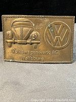 Photo of the worn brass rectangular Volkswagen belt buckle showing Beetle car front, VW logo, and text 'Volkswagenwerk AG Wolfsburg'