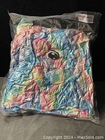 Folded colorful children's unicorn bathrobe with pastel rainbow colors showing an eye design, sealed in clear plastic packaging.