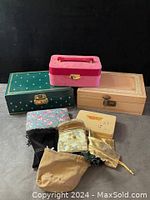 Five jewelry boxes stacked and set on a surface with multiple string-tie fabric jewelry bags placed in front.