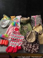 Photo showing various dog clothes including a pink unicorn sweater, red and white knit sweater, green jacket with skull patch, black bone pattern vest, beige jacket, and orange rain boots.