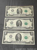 Lot of three US two dollar bills laid flat on a black surface, showing the front side with varying serial numbers and Federal Reserve seals.
