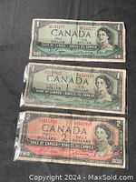 Front views of three Canadian banknotes including two green $1 bills and one red $2 bill, all showing Queen Elizabeth II.