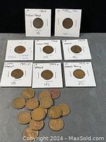 Eight coins in labeled 2x2 holders arranged in rows with a pile of loose pennies below