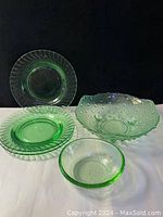 Three pale green glass plates and two unique pale green bowls displayed on black background