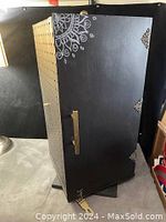 Black vertical rotating jewelry display cabinet with decorated door and handle.