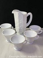 Milk glass pitcher and five matching cups showing grapevine relief pattern.