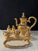 Full tea set arranged with tea pot, cream and sugar pitchers, salt and pepper shakers, and serving tray.