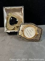 Silver belt buckle with detailed engraving and large black-and-gold spade trinket box with heart detail.