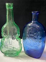 Two glass bottles shown: green violin-shaped bottle and blue oval bottle with sailing ship and American flags