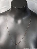 Necklace shown on black mannequin bust highlighting length and delicate twisted style in natural light.
