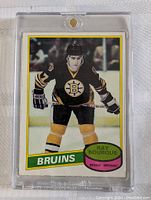 Front view of the 1980-81 O-Pee-Chee Ray Bourque rookie hockey card in a sturdy clear protective case, showing Bourque in Bruins uniform skating on ice.