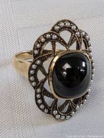 Front view showing central domed black tourmaline and surrounding seed pearls