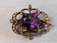 Front view of the brooch showing oval faceted amethyst and seed pearl-set scrolling frame