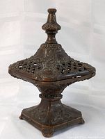 Front angled view of antique bronze incense burner, showing detailed lid with open lattice design and ornate embossed patterns.