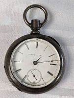 Front face of the antique Illinois pocket watch showing the white dial with Roman numerals and small subsidiary seconds dial.