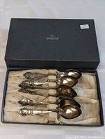 Six antique silver spoons displayed in a lined presentation box with Smith Brothers Jewelers Kingston branding. The spoons show a sports theme on handles, possibly lawn bowling.