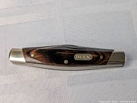Closed view of Buck 373 folding knife showing wooden handle with metal engraved Buck emblem and metal bolsters.