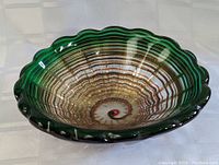 Top-down image showing the art glass bowl's intricate amber swirl interior pattern with scalloped dark green rim.