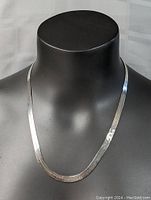 Sterling silver necklace displayed on black mannequin showcasing length and flat band design.