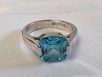 Close-up of square-cut blue gemstone on sterling silver ring, showing engraved marking inside band.