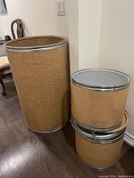 Set of three round storage bins; one large and two smaller nested bins, all with brown exteriors and metal rims.