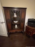 Full view of the wooden buffet showing the glass front door with three shelves inside and decorative carvings.