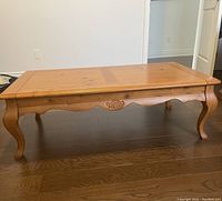Side view of a wooden coffee table showing carved detailing on apron and curved legs.