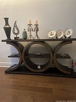 Full view of the console table showing the wood structure with circular shelving and some decorative items on top and in shelves.