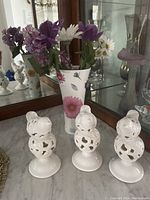 Three white ceramic bird figurines and a floral ceramic vase with artificial flowers on a mirrored surface.