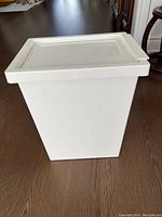 White plastic rectangular storage bin with hinged lid sitting on wood floor, lid closed.