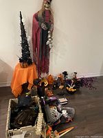 Wide shot showing all Halloween decorations including skeleton, lighted tree, pumpkins, and crate of masks and props on floor.
