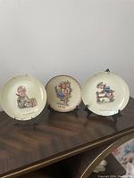 Front view of three M.J. Hummel collector plates on stands