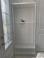 Full view of white metal laundry hanging organizer mounted between door and wall near a frosted glass window.