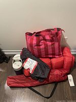 Shot of all camping items including the sleeping bag in its carry bag, two red camping beds, outdoor chair carry bag, and insulated drink container.