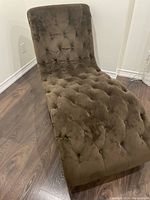 Front angle view showing the velvet tufted upholstery and curved shape of the lounge chair on dark wood flooring.