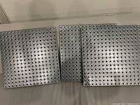 Three metal pegboard panels arranged side-by-side on a surface showing diamond pattern of holes.