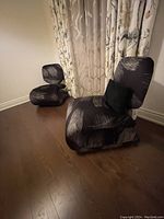 Two modern upholstered lounge chairs placed on wooden floor near window with floral curtains.