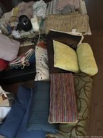 Photo showing assorted pillows, rugs, a garment steamer, and other bedding and bathroom accessories arranged on a surface.