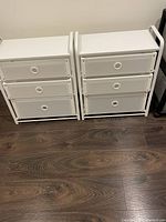 Two white plastic drawer storage units side by side, three drawers each, on wood flooring